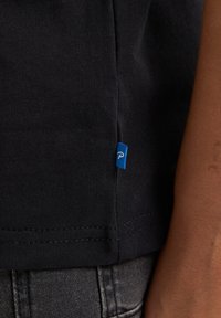 Camiseta de algodón negra con una etiqueta lateral azul. Presenta un escote redondo sencillo y mangas cortas, con una textura suave y costuras limpias.