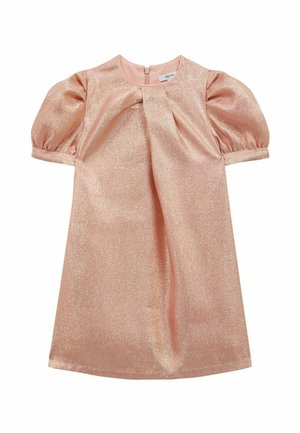 Jong meisje met donker haar in een knot, gekleed in een glanzende lichtroze jurk met pofmouwen en beige Mary Jane schoenen, staand tegen een witte achtergrond.