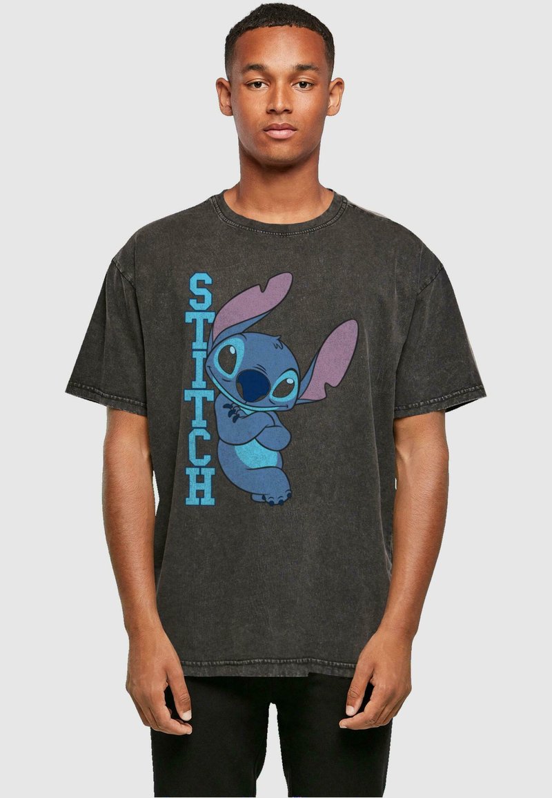T-shirt en coton gris surdimensionné avec un personnage de dessin animé bleu et violet, accompagné du texte "STITCH" en gras bleu à côté.