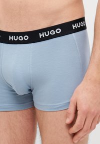 Világoskék boxer nadrág fekete elasztikus derékpánttal, amelyen fehér "HUGO" márkázás található. Az anyag simának tűnik, és testhez simuló kialakítású.