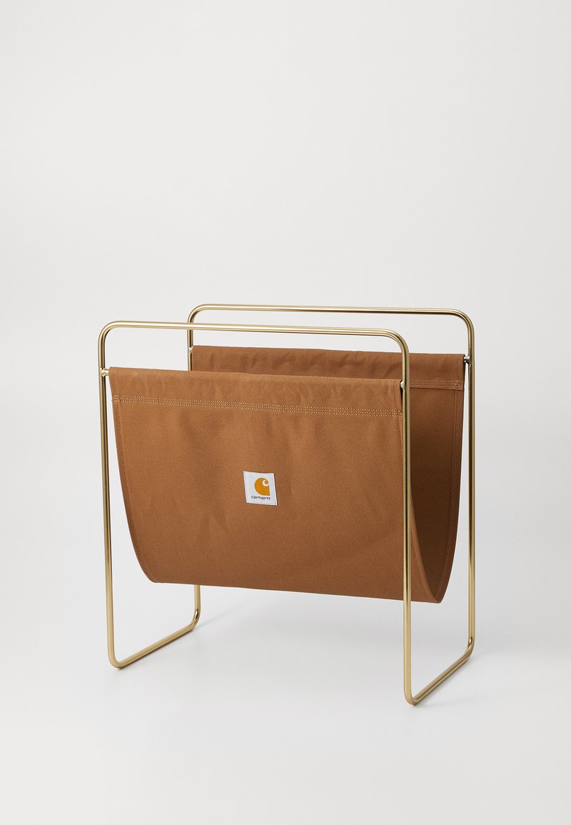 Smeđa tkanina za časopise s zlatnim metalnim okvirom, koja sadrži oznaku s logotipom. Dizajn je minimalistički s glatkim linijama i mekanom teksturom.