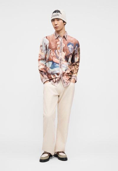 Πουκάμισο: μακρυμάνικο με πολύχρωμο εκτυπωμένο σχέδιο; κουμπιά μπροστά. Παντελόνι: φαρδύ, μπεζ ύφασμα. Αξεσουάρ: πλεκτός μπεζ σκούφος, παπούτσια με σχέδιο.