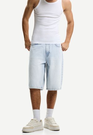 Jasnoniebieskie szorty dżinsowe o luźnym kroju, z prostymi nogawkami i kieszeniami po bokach, zestawione z białym topem na ramiączkach i beżowymi trampkami.