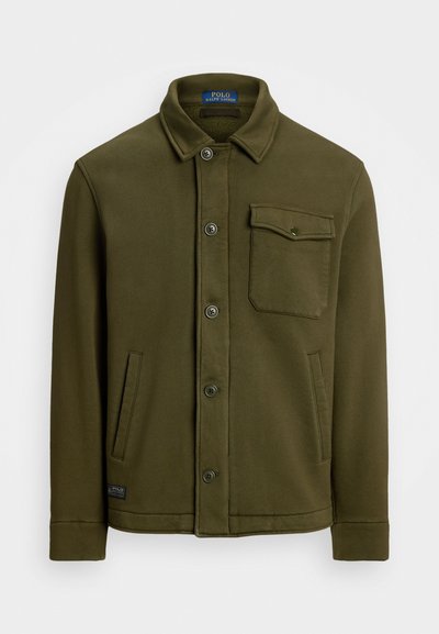 Casaco de algodão verde oliva escuro, com colarinho, botões à frente, um bolso no peito e dois bolsos laterais. Textura suave com detalhes mínimos.