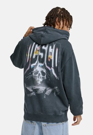 Grafitowa bluza z kapturem z dużym nadrukiem przedstawiającym czaszkę i błyskawicę. Na plecach tekst "DCSC" w pogrubionych, kolorowych literach.