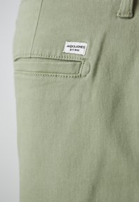 Jasnozielone spodnie wykonane z miękkiego materiału, z przeszytą kieszenią, na której znajduje się biała metka z napisem "JACK & JONES" oraz "EST.1990."