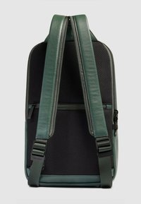 Groene leren rugzak met zwarte mesh achterkant, voorzien van verstelbare riemen en een ritsvak aan de voorkant voor opslag.