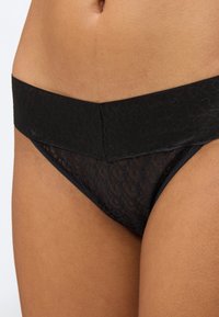 Primo piano di una persona che indossa biancheria intima nera con motivo in pizzo e una larga fascia in vita nera e solida, che mostra l'addome inferiore e la parte superiore delle cosce.