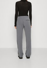 Pantalons large gris avec une taille élastique, en tissu lisse, dotés d'une seule poche arrière et tombant jusqu'à la cheville.