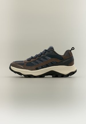 Dunkelbrauner und marineblauer Mesh-Wanderschuh mit dicker weißer Sohle und schwarzem Profil, mit Zuglasche und Merrell-Logo an der Seite.