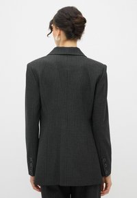 Blazer nero a righe con una silhouette strutturata, ampi rever e dettagli a tre bottoni sulle maniche. Finitura in tessuto liscia.