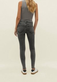 Jeans ajustados de talle alto en gris con dos bolsillos traseros, combinados con una blusa sin mangas en gris y zapatillas blancas con detalles en negro.