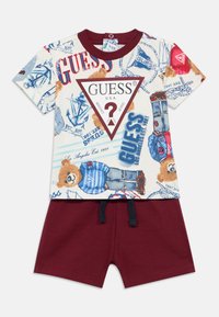 Μπλουζάκι με πολύχρωμη εκτύπωση αρκούδας και κειμένου, κόκκινο τριγωνικό λογότυπο· σετ με κόκκινα σορτς με ελαστική μέση και κορδόνι.