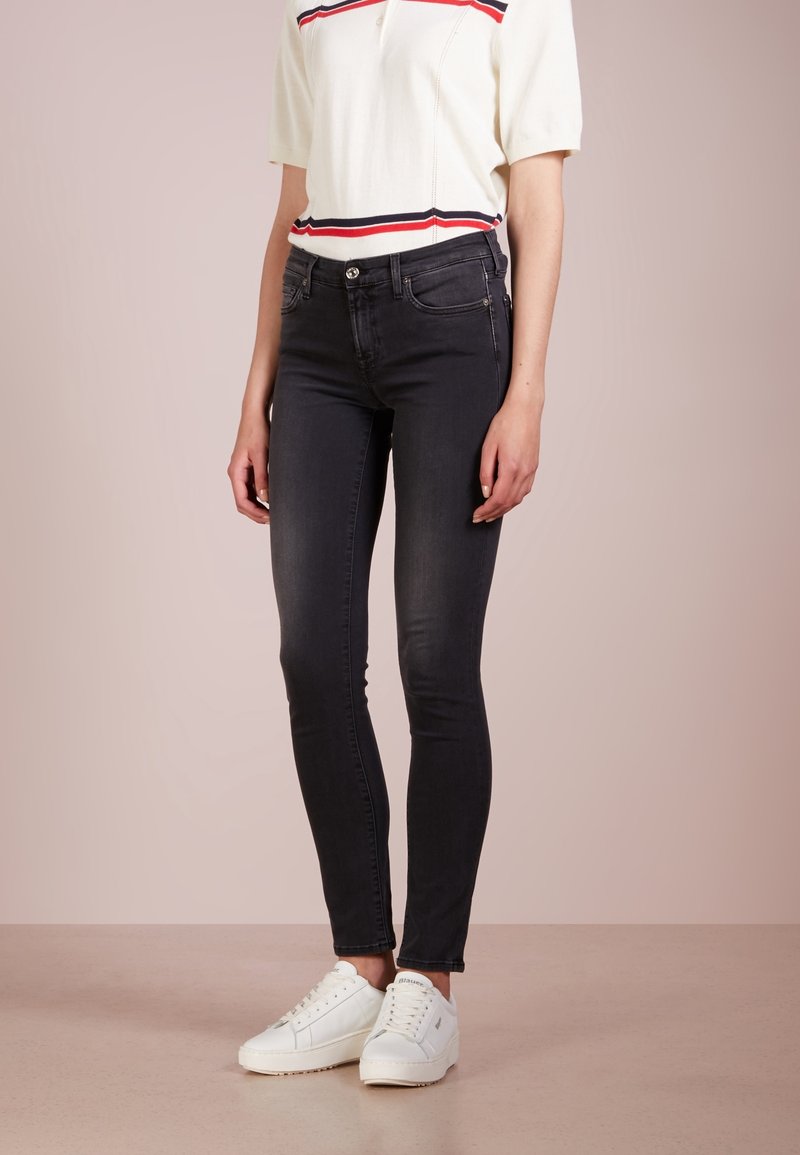 Zwarte skinny jeans met een gladde textuur, voorzien van klassieke vijf-pocketstijl, gecombineerd met een wit en rood gestreept gebreid T-shirt en witte sneakers.