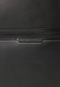 Juoda tekstūruota odinė rankinė su viršutiniu užtrauktuku ir įspauduotu "Armani Exchange" logotipu, su subtiliais sidabro akcentais ir siuvimo detalėmis.
