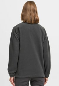 Tumehall villane sweatshirt pikkade varrukatega ja lõdva lõikega. Sile tekstuur ribitud mansettide ja servaga, ilma eristuvate mustrite või aksessuaarideta.