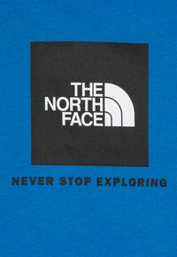 Mėlynasis medvilninis marškinėliai su juodu kvadrato dizainu ir baltu užrašu "THE NORTH FACE" bei "NEVER STOP EXPLORING" po juo.