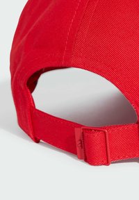 Cappello da baseball rosso con un tessuto texturizzato. Presenta una fascia regolabile sul retro con una fibbia in plastica. Niente motivi o loghi visibili.