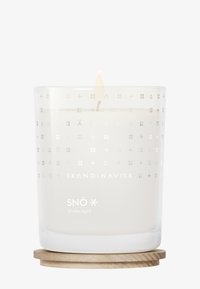 Tændt hvidt lys mærket "SNÖ Vinterlys" i en gennemsigtig glasholder med nordiske symboler, hviler på en rund træunderlag.