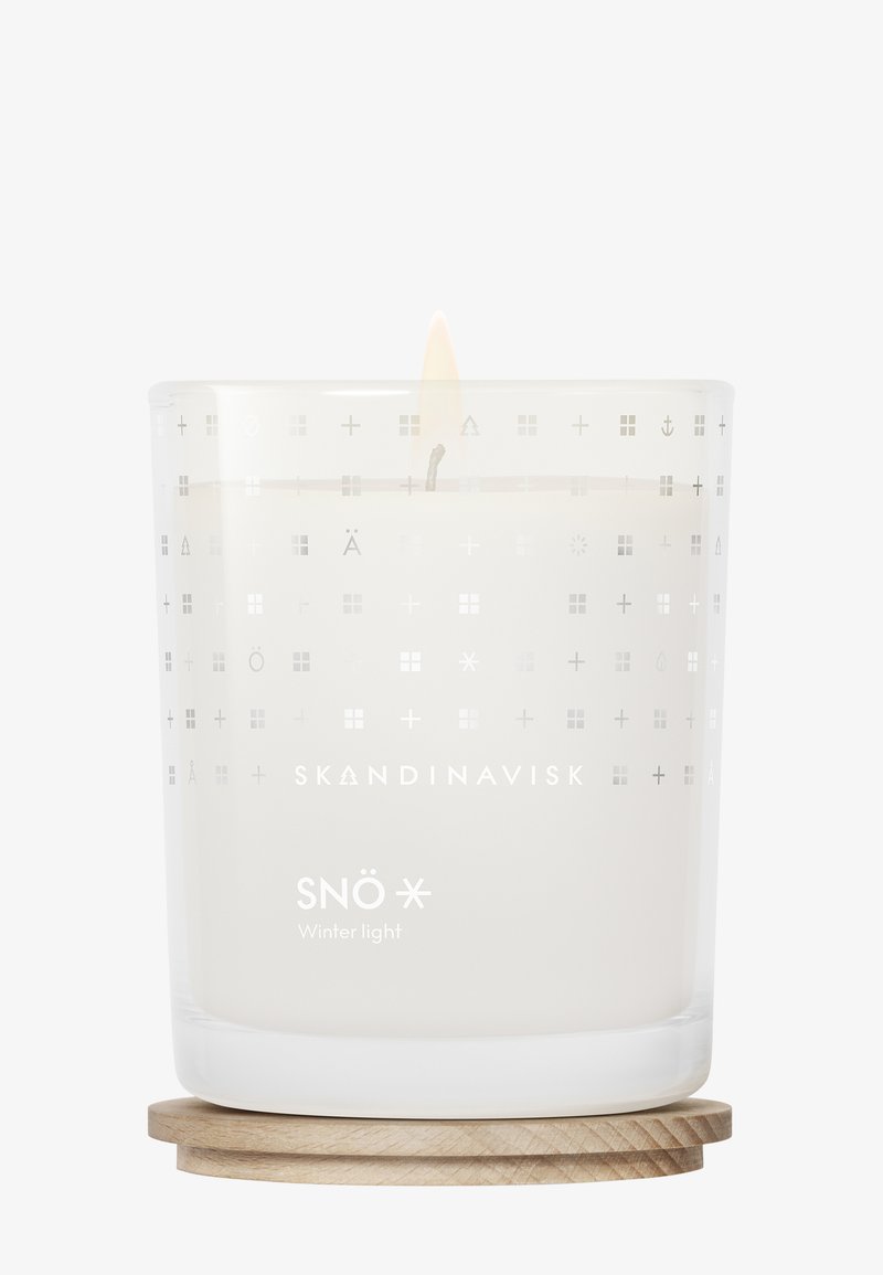 Tændt hvidt lys mærket "SNÖ Vinterlys" i en gennemsigtig glasholder med nordiske symboler, hviler på en rund træunderlag.