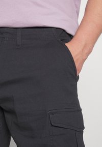 Pantalones cargo de color gris oscuro con corte recto, que cuentan con bolsillos laterales y una cinturilla visible, fabricados con una resistente mezcla de algodón.