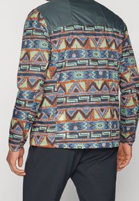 Multifarvet mønstret skjorte med geometriske designs i brun, grøn og blå. Tekstureret stof med en ensfarvet mørkegrøn yoke.