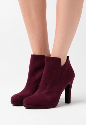 Bottines en suède bordeaux avec un bout arrondi, un talon haut et des découpes sur les côtés pour un design épuré. Fini en matériau texturé.
