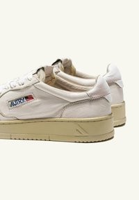 Sneakers bianche in pelle con finitura testurizzata, lacci piatti e suole in gomma beige. Presentano una toppa con logo con accenti rossi e blu.