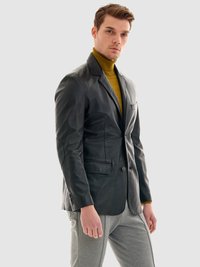 Svart läderblazer med strukturerade axlar, snedskurna slag, enstaka knappstängning och framfickor, bärs över en senapsgul polotröja.