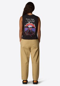 Camiseta sin mangas negra con un gráfico colorido de montañas y figuras, combinada con pantalones beiges y zapatos negros con acentos naranjas.