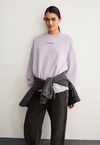 Lavender sweatshirt met geborduurd "ARMEDANGELS" in het blauw. Gecombineerd met donkergrijze, losse broek en een spijkerjack om de taille geknoopt.