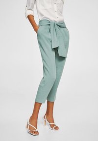 Pantalons courts vert clair en tissu texturé, dotés d'un lien à la taille et de poches latérales, associés à des talons blancs à lanières.