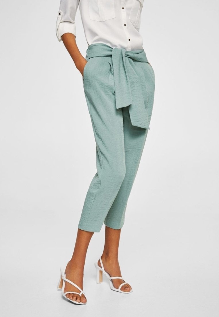 Pantalons courts vert clair en tissu texturé, dotés d'un lien à la taille et de poches latérales, associés à des talons blancs à lanières.