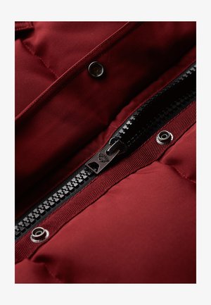 Burgunderfarvet pufferjakke med en sort lynlås, sølvknapper og en quiltet tekstur, der fremhæver et blødt og glat ydermateriale.