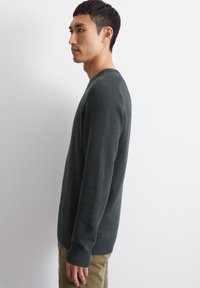 Dark green textured sweater with a crew neck, ribbed cuffs, and hem, featured on a side view model against a white background.