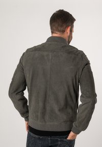 Giacca bomber da uomo realizzata in suede verde oliva con colletto e polsini a costine, caratterizzata da una texture liscia e un design aderente.