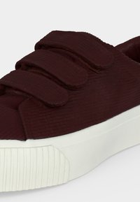 Baskets marron foncé avec trois larges bandes velcro et une épaisse semelle en caoutchouc blanche texturée.