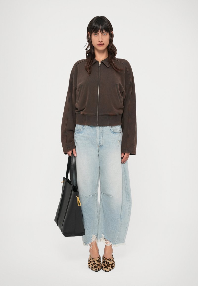 Brūna īsa rāvējslēdzēja jaka, gaiši zili, nodiluši plaša piegriezuma džinsi, leoparddrukas mulei un melna tote soma ar zelta detaļām.