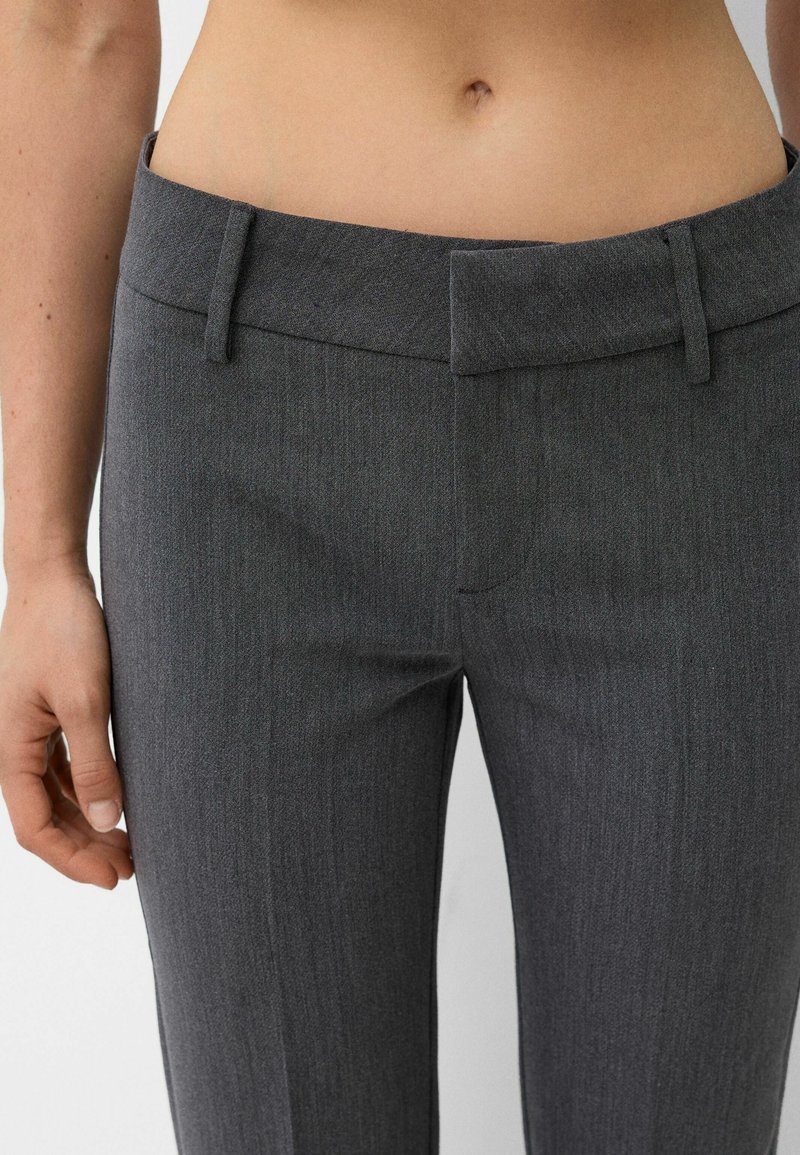 Pantaloni grigi sartoriali con una texture liscia, frontale piatto e passanti per cintura. Presentano una vestibilità slim e un sottile dettaglio a righe.