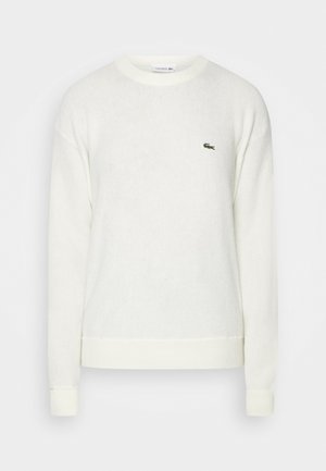 Biały sweter z okrągłym dekoltem, wykonany z miękkiego materiału. Posiada ściągacze na mankietach i dołem. Małe zielone logo Lacoste na piersi. Prosty, klasyczny design.