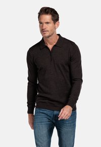Dunkelbrauner Pullover mit einem Reißverschlusskragen, langen Ärmeln und gerippten Bündchen, kombiniert mit blauen Jeans, was einen lässigen, aber eleganten Look zeigt.