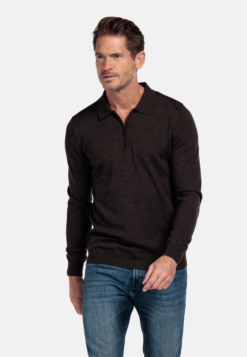 Dunkelbrauner Pullover mit einem Reißverschlusskragen, langen Ärmeln und gerippten Bündchen, kombiniert mit blauen Jeans, was einen lässigen, aber eleganten Look zeigt.