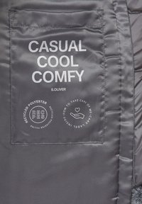 Étiquette de poche sur un tissu gris avec le texte "CASUAL COOL COMFY" et des icônes circulaires indiquant du polyester recyclé et des instructions d'entretien.