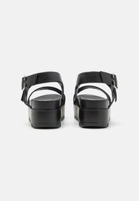 Black platform sandals featuring a smooth leather upper, adjustable ankle strap with buckle, and a contoured footbed for support.