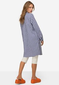 Vestito camicia a quadri blu e bianchi con maniche lunghe, lunghezza al ginocchio, realizzato in tessuto leggero. Abbinato a pantaloni cropped crema e sandali platform arancioni.