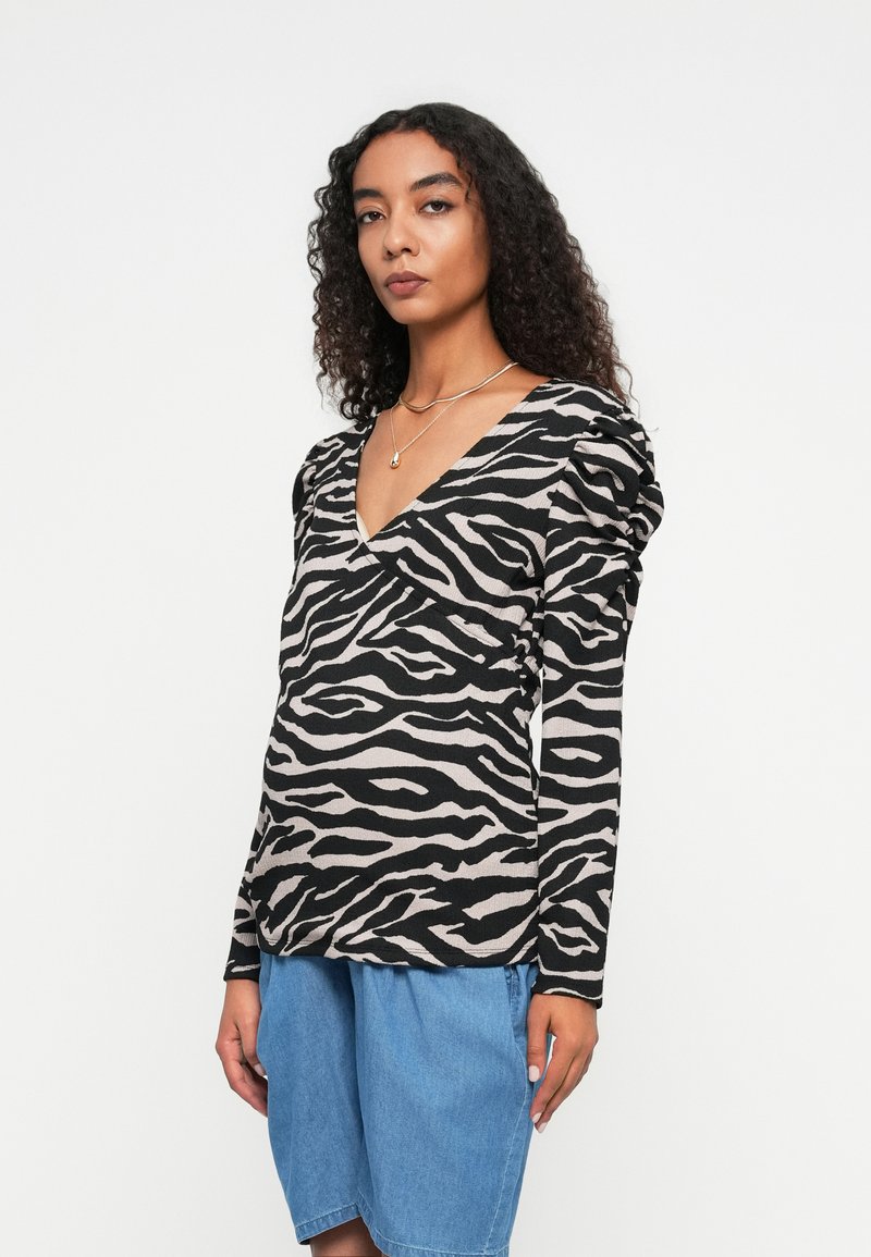 Langärmliges Oberteil im Schwarz-Beige-Zebra-Print, mit V-Ausschnitt und gerafften Schulterdetails, kombiniert mit Jeansshorts.