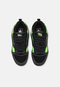Mustat ja neonvihreät Vans-tennarit mustilla nauhoilla, valkoisella ompeleella ja "Off The Wall" -logolla kielekkeellä, kuvattuna ylhäältä valkoista taustaa vasten.