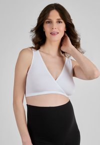 Balta, minkšta medžiaga liemenėlė su apvyniojimo dizainu ir banguotu kraštu, derinama su juodomis kelnėmis su aukštu liemeniu. Minkšta tekstūra.