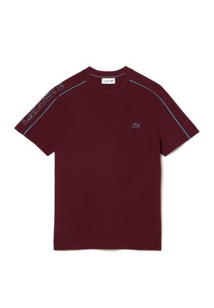 T-shirt bordeaux à manches courtes avec passepoil bleu clair sur les épaules, lettrage Lacoste sur la manche gauche et petit crocodile brodé sur la poitrine.