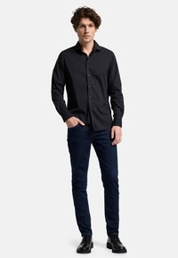 Svart skjorta med knappslå, krage, långa ärmar och en figursydd design, kombinerad med mörkblå jeans och svarta läderskor.